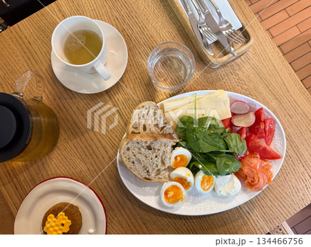 Morning meal with tea, honey dessert, eggs, vegetables, cheese, and bread arranged on wooden surface top view. Balanced breakfast symbolizing comfort and slow living. Morning meal with tea, honey dessert, eggs, vegetables, cheese, and bread arranged on wooden surface top view. Balanced breakfast symbolizing comfort and slow living. 134466756