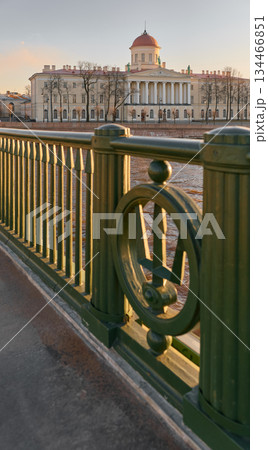 view through the metal wrought iron railing with a trident on the Birzhevoy bridge to the institute of Russian Literature at sunset, lampposts on the bridge, Neva River, Vasilyevsky Island view through the metal wrought iron railing with a trident on the Birzhevoy bridge to the institute of Russian Literature at sunset, lampposts on the bridge, Neva River, Vasilyevsky Island 134466851