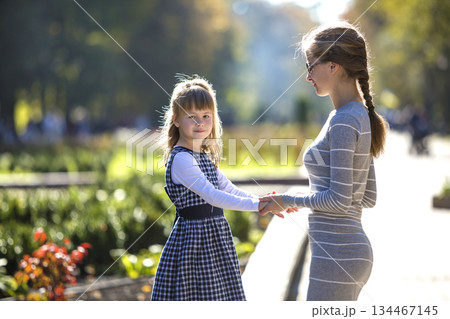 Back view of child girl and mother in dresses together holding hands on warm day outdoors on sunny background. Back view of child girl and mother in dresses together holding hands on warm day outdoors on sunny background. 134467145