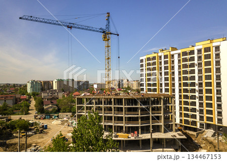 Apartment or office tall building under construction. Working builders and tower cranes on bright blue sky copy space background. Apartment or office tall building under construction. Working builders and tower cranes on bright blue sky copy space background. 134467153