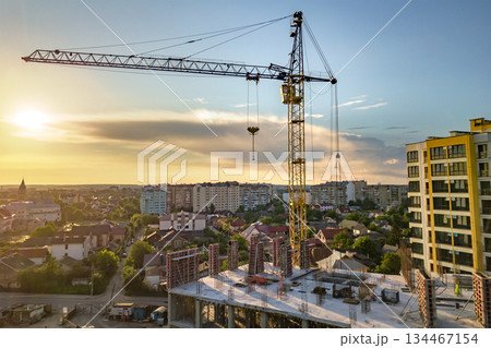 Apartment or office tall building under construction. Brick walls, glass windows, scaffolding and concrete support pillars. Tower crane on bright blue sky copy space background. 134467154