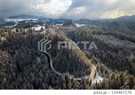 Aerial view of winter landscape with snow covered mountain hills and winding forest road in morning. Aerial view of winter landscape with snow covered mountain hills and winding forest road in morning. 134467176