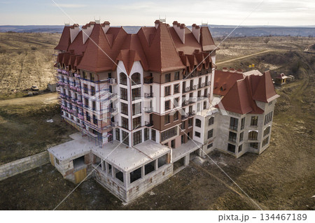 Aerial view of unfinished multistoried residence, hotel or cottage building with stucco wall, cast iron balcony railings, steep shingle roof and shiny windows on rural landscape background. Aerial view of unfinished multistoried residence, hotel or cottage building with stucco wall, cast iron balcony railings, steep shingle roof and shiny windows on rural landscape background. 134467189
