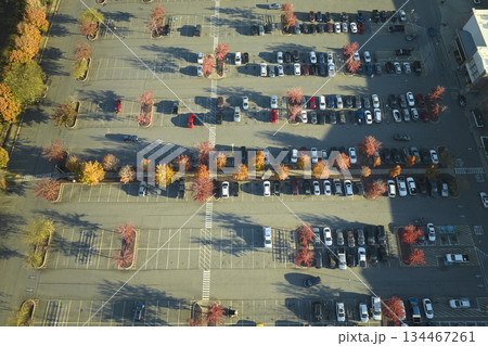 Aerial view of many colorful cars parked on parking lot with lines and markings for parking places and directions. Place for vehicles in front of a strip mall plaza Aerial view of many colorful cars parked on parking lot with lines and markings for parking places and directions. Place for vehicles in front of a strip mall plaza 134467261