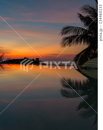 View from luxury villa at dusk, pool lighting, sun loungers for sunbathing, umbrellas from the sun, pillows for swimming in the pool, palm tree on background 134468133