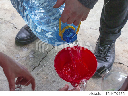 A man pours clean drinking water from a large container into a bottle using a funnel. Close-up. A man pours clean drinking water from a large container into a bottle using a funnel. Close-up. 134470423