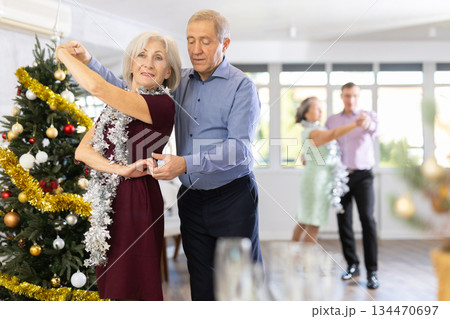 Smiling elderly woman and partner successfully perform mesmerizing movements of paso doble dance during celebration Christmas and New Year Smiling elderly woman and partner successfully perform mesmerizing movements of paso doble dance during celebration Christmas and New Year 134470697