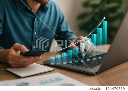 AI generated digital business growth with a man reviewing rising holographic bar charts using a laptop and smartphone in a warm modern workspace 134470769