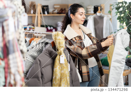 Young woman chooses down jacket in clothing store Young woman chooses down jacket in clothing store 134471298