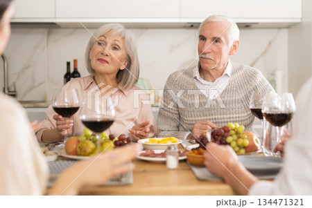 Mature married couple are sitting at table, enjoying food and wine with middle-aged guests. 134471321