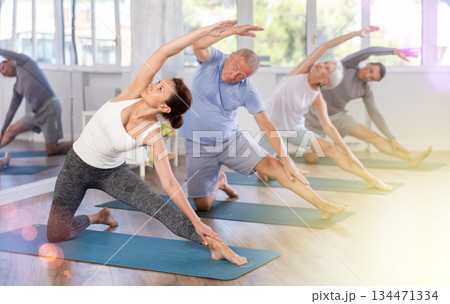 Girl performs Parighasana, bolt pose with mature yoga amateurs Girl performs Parighasana, bolt pose with mature yoga amateurs 134471334