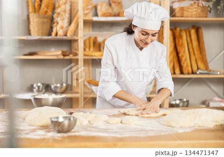 Young woman works as baker, mold baguette from dough, creates long loafs from dough. 134471347