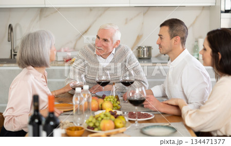 Senior parents and young couple sitting at table drinking wine and having conversation Senior parents and young couple sitting at table drinking wine and having conversation 134471377