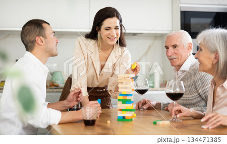 Joyful senior parents and young couple sitting around table playing brick game 134471385
