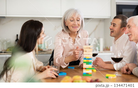 Joyful senior parents and young couple sitting around table playing brick game Joyful senior parents and young couple sitting around table playing brick game 134471401