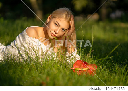Young woman resting on green grass with flowers nearby Young woman resting on green grass with flowers nearby 134471483