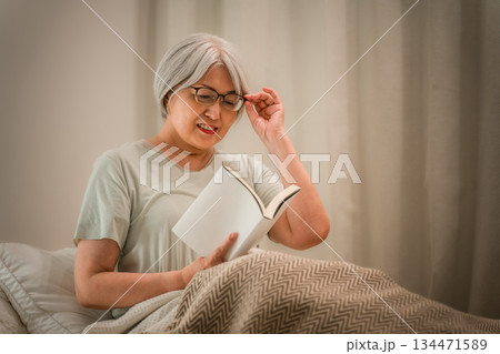 ベッドルームでおやすみ前に読書をするグレイヘアのシニア女性 134471589