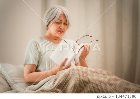 ベッドルームでおやすみ前に読書をするグレイヘアのシニア女性 134471590