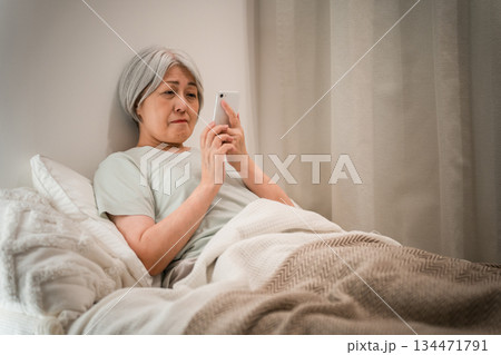 ベッドルームでおやすみ前にスマホを見るグレイヘアのシニア女性（困る,心配,不安,悩み） 134471791