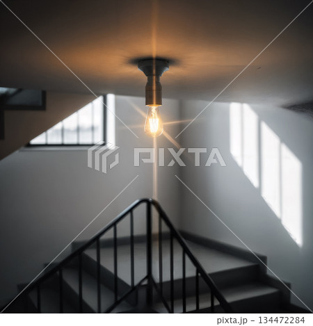 lonely light bulb shines on the ceiling in a minimalist entrance with stairs and shadows 134472284