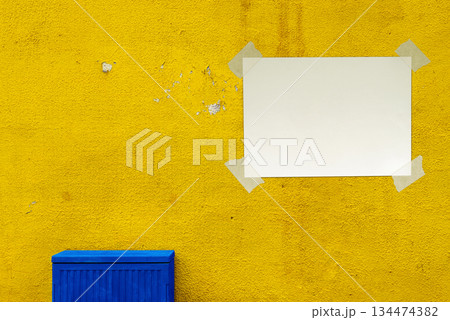 Blank Paper Sheet with Adhesive Tape on a Yellow Wall Featuring a Textured Surface. File with Clipping Path. 134474382