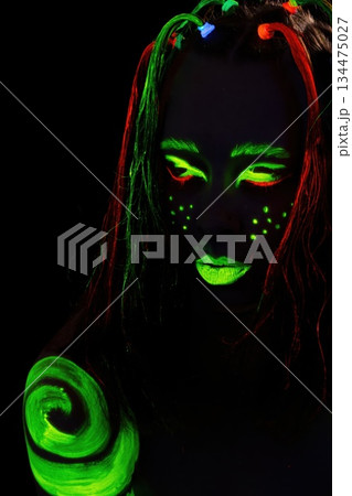 Woman displays neon body art and makeup in the dark setting for colorful, unique portrait Woman displays neon body art and makeup in the dark setting for colorful, unique portrait 134475027