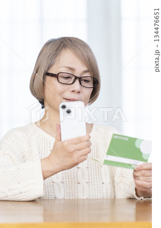 リビングでスマホと通帳を見るシニア女性 リビングでスマホと通帳を見るシニア女性 134476651