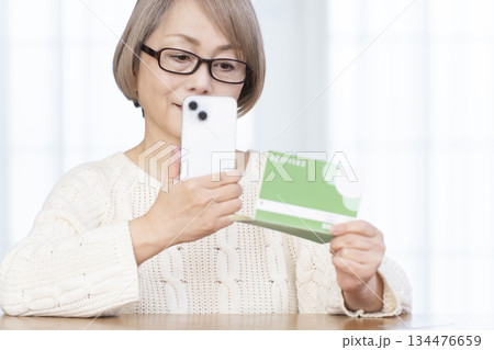 リビングでスマホと通帳を見るシニア女性 リビングでスマホと通帳を見るシニア女性 134476659