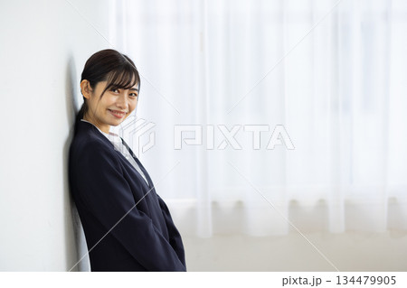 白い壁にもたれて微笑むスーツ姿の若い日本人女性ビジネスパーソン 134479905