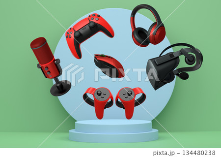 Assorted gaming gadgets like controllers, VR headset, mouse, and mic floating above circular podium and white platform 134480238