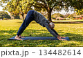 Senior Caucasian man performs yoga exercises on a mat in a sunny meadow in a morning park, a sport for the health and longevity of older people 134482614