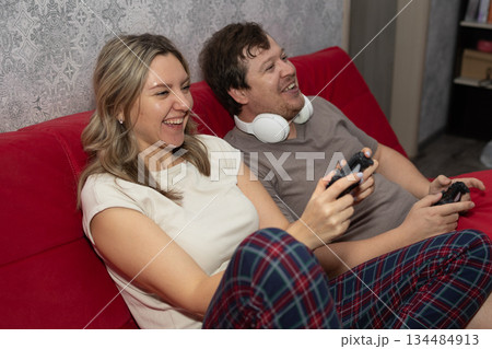 Happy Couple Playing Video Games on a Red Couch at Home in the Evening 134484913