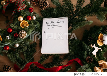 Blank New Years resolution list on a notepad surrounded by festive evergreen decorations. Goal setting, personal growth, mental health reflection, seasonal motivation Blank New Years resolution list on a notepad surrounded by festive evergreen decorations. Goal setting, personal growth, mental health reflection, seasonal motivation 134485176