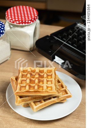 Stack of Homemade Viennese Waffles on a Table with an Electric Waffle Maker 134485864