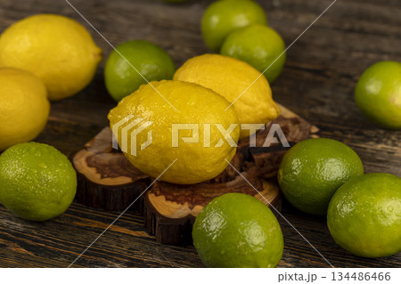 wet yellow sweet and sour lemon and green limes lying on the table, ripe citrus fruits lemons and limes lying on a table covered with drops of water 134486466