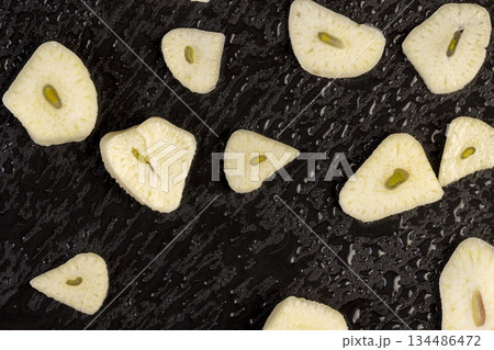 freshly peeled and sliced garlic scattered on black slate, peeled and sliced fragrant natural and fresh spices from garlic cloves scattered on black slate stone, covered with drops of water 134486472