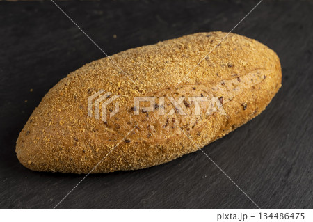 a soft loaf of bread on black slate, a freshly baked soft loaf of rye bread lies on the table a soft loaf of bread on black slate, a freshly baked soft loaf of rye bread lies on the table 134486475