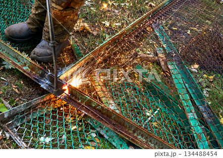A cleaner. A worker cuts metal construction waste with a gas torch A cleaner. A worker cuts metal construction waste with a gas torch 134488454