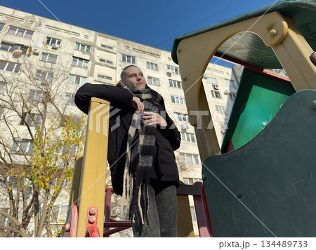Young woman urban playground stands pensively against apartment buildings on a cold day. Young woman urban playground stands pensively against apartment buildings on a cold day. 134489733