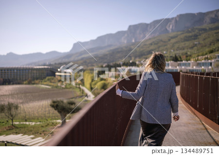 Woman walking mountains railing overlooking vast scenic landscape and modern resort 134489751