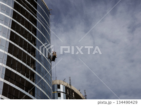 Construction worker on a suspended cradle Construction worker on a suspended cradle 134490429