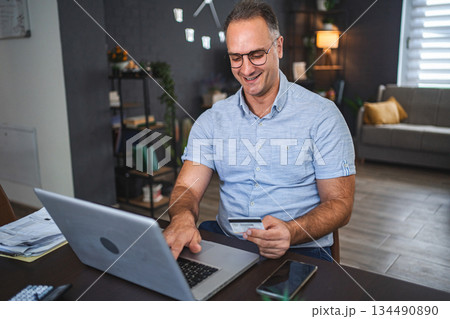Middle aged Caucasian man online shopping on laptop at home 134490890