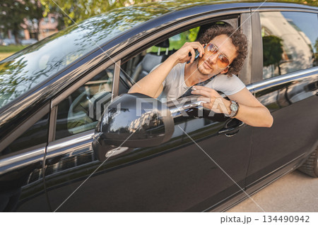 Man with curly hair using phone and looking in the rearview mirror Man with curly hair using phone and looking in the rearview mirror 134490942