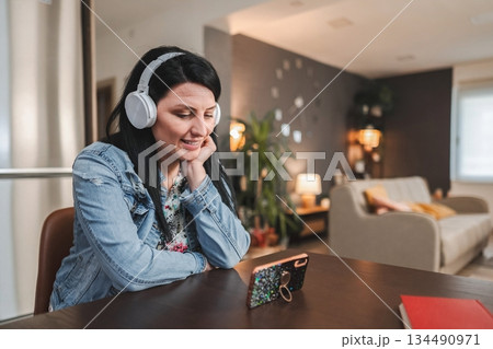 Woman wearing headphones attending a video call on smartphone at home 134490971