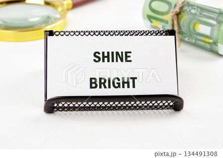 A message stating SHINE BRIGHT rests near rolled Euros and a magnifying glass, hinting at financial prosperity and promising future opportunities A message stating SHINE BRIGHT rests near rolled Euros and a magnifying glass, hinting at financial prosperity and promising future opportunities 134491308