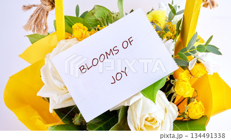 A colorful gathering of white roses and petite yellow roses are nestled in bright yellow wrapping with greenery, a delightful presentation showing Blooms of Joy 134491338