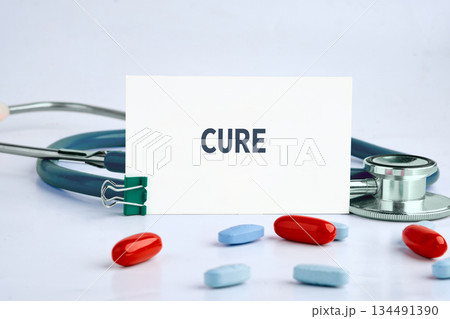 A white card displaying the word CURE is nestled among red and blue pills and a stethoscope, conveying health and medical treatment concepts A white card displaying the word CURE is nestled among red and blue pills and a stethoscope, conveying health and medical treatment concepts 134491390