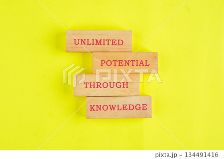Four wooden blocks, arranged vertically, state UNLIMITED, POTENTIAL, THROUGH, and KNOWLEDGE, showcasing education on a vibrant yellow surface 134491416