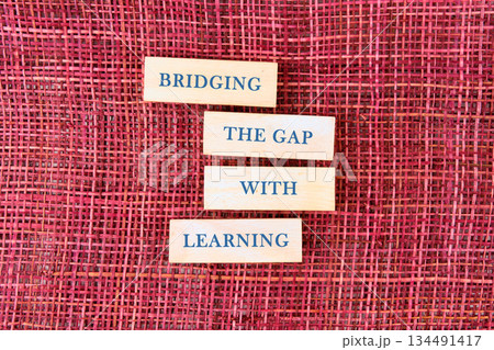 Wooden blocks with the words BRIDGING THE GAP WITH LEARNING are aligned vertically. The textured, woven surface provides a vibrant crimson backdrop Wooden blocks with the words BRIDGING THE GAP WITH LEARNING are aligned vertically. The textured, woven surface provides a vibrant crimson backdrop 134491417