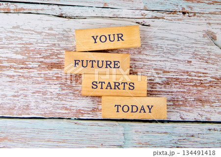 Four wood blocks are stacked on a rustic white surface with the inspiring phrase YOUR FUTURE STARTS TODAY spelled out on them. A powerful motivation statement 134491418
